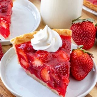whipped cream topped strawberry pie with strawberry next to slice.