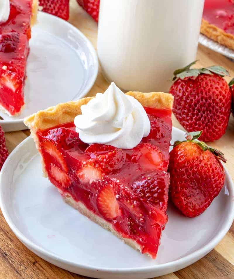 Strawberry pie on plate with whipped cream and milk on side